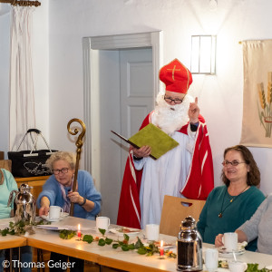 Ein verkleideter Nikolaus steht an einem Tisch mit Menschen und hebt den Zeigefinger