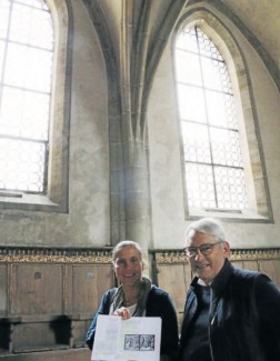 Martina Knodt und Dietrich Kappler von den Spitalkirchenöffnern zeigen eine Kopie des Dokuments, das die beiden entfernten farbigen Glasfenster beschreiben und abbilden, die einmal auf der Chornordseite über ihnen eingebaut waren.